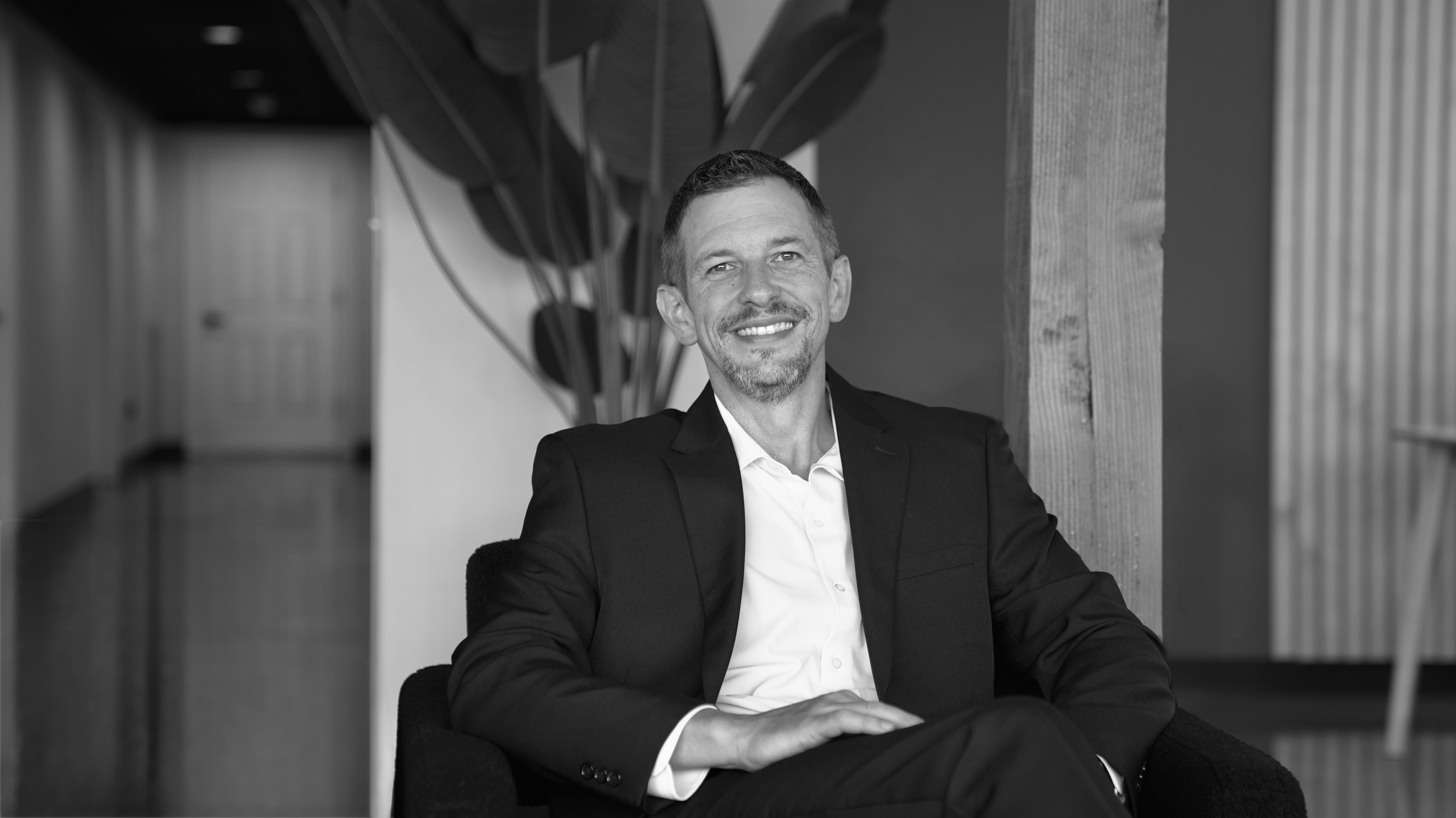 Jeremy Godwin seated in a suit, smiling for a black and white portrait.